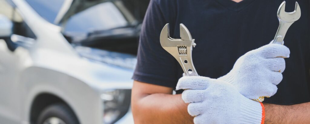 man standing in front of a car, holding wrenches