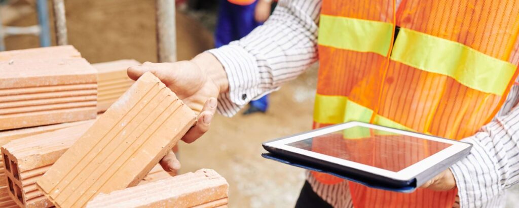 a man holding a tablet and examining red bricks