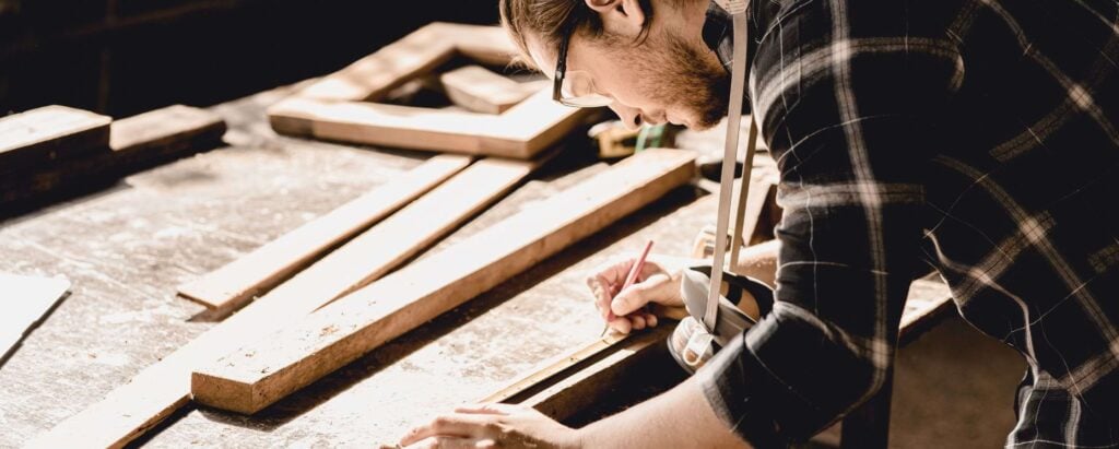 a man with goggles measuring out wood
