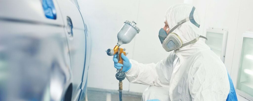 a man in a white suit spray painting a car