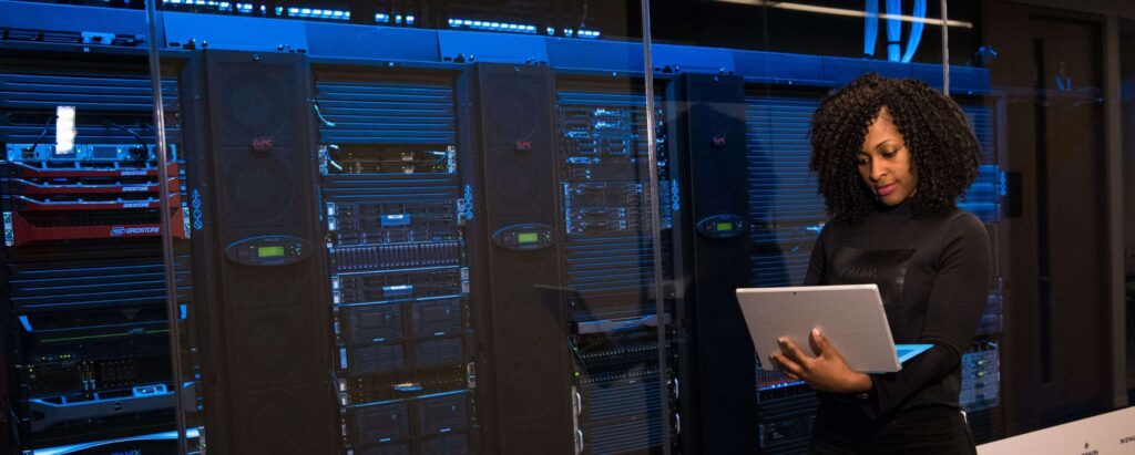 a woman looking at a laptop, standing in front of server racks