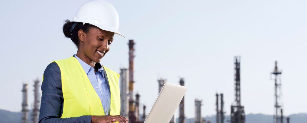 a woman looking at her laptop, with chemical factories behind her