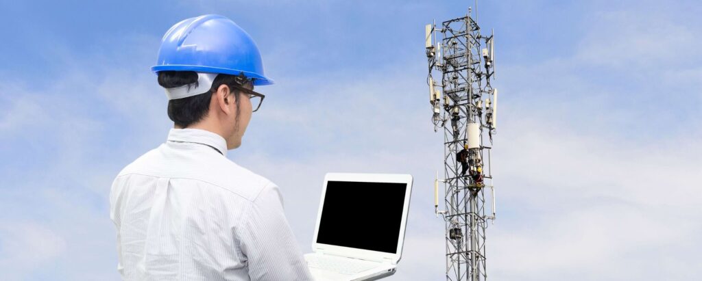 telecommunications equipment worker with a laptop standing in front of a telecommunications tower