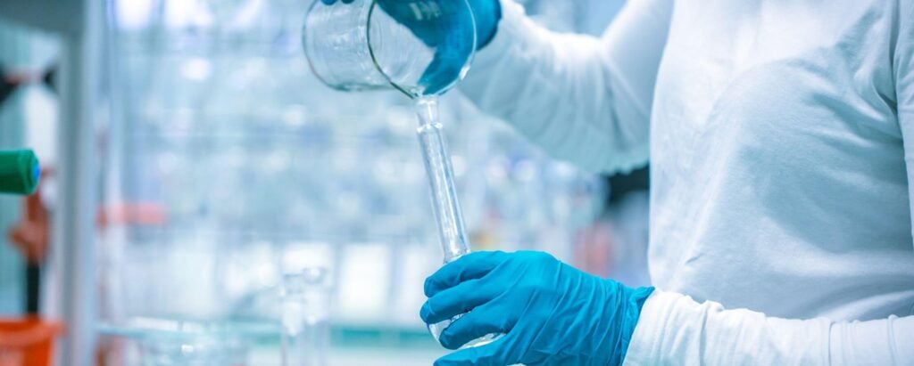 a scientist pouring liquid in a glass container