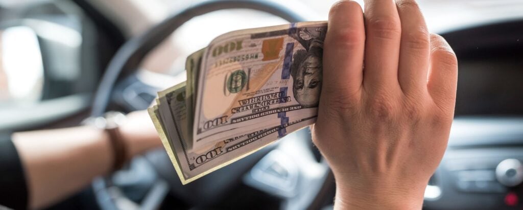 person holding a wad of cash whilst driving a car