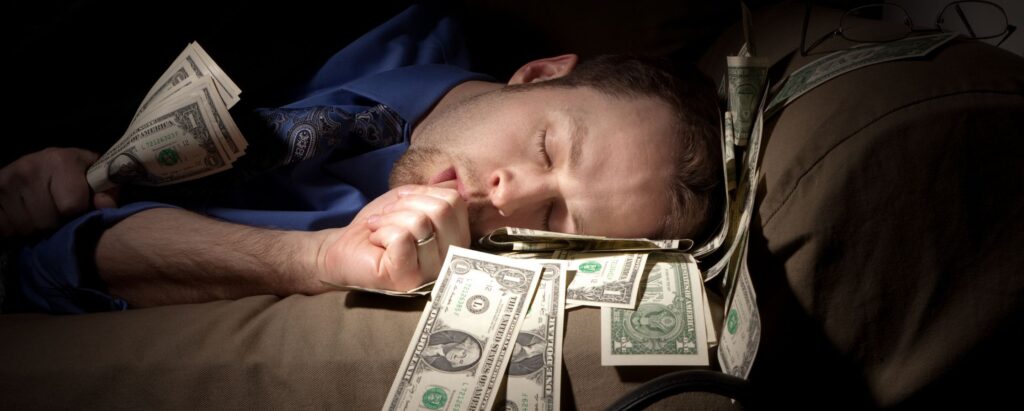Man sleeping in bed while holding a wad of money in his hand