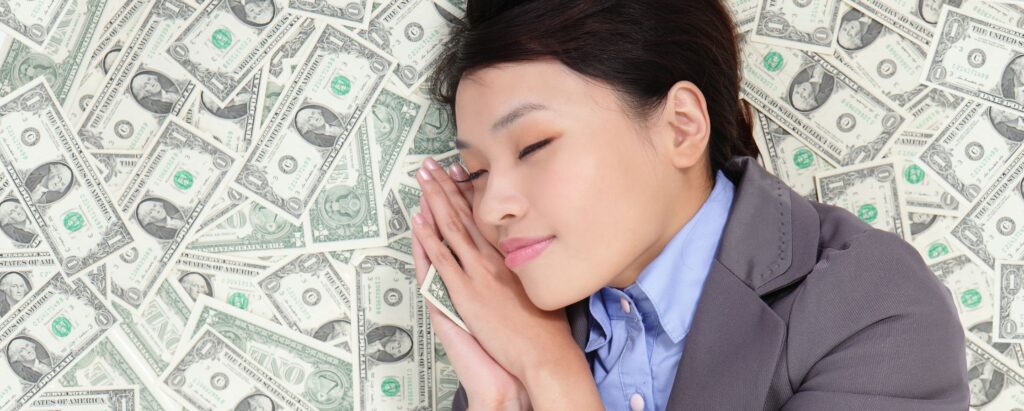 A girl sleeping on a floor full of money with a happy smile on her face