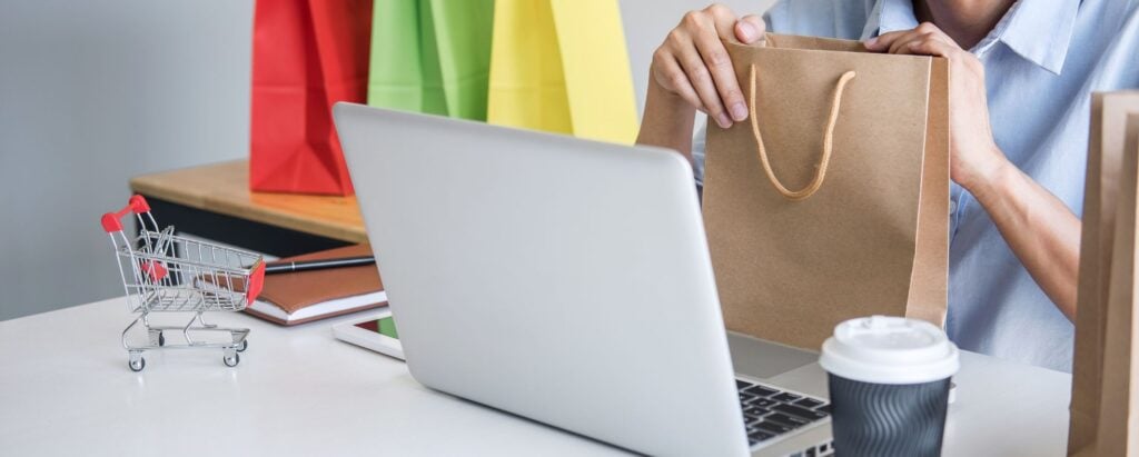 Person holding a shopping bag in front of the computer, earning money by shopping