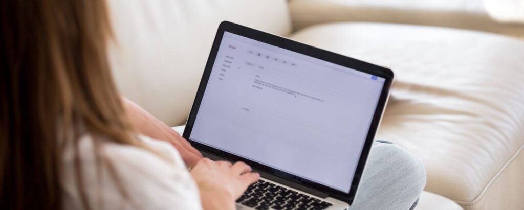 A girl reading an email on a laptop while sitting on a sofa