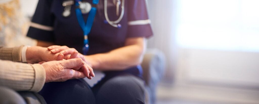 Home nurse sitting with an older patient on sofa and holding his hands